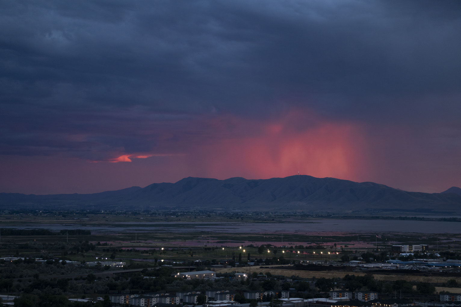 The sheets of rain over the mountain catch the red sunset light and glow, a red mist in the otherwise blue cloudy sky